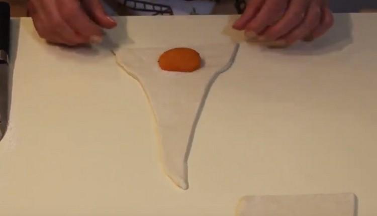 Ant plačios trikampio dalies užpilkite šiek tiek cukraus ir paskleiskite pusę abrikoso.