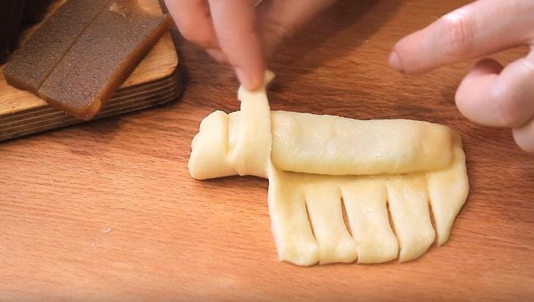 Effettuando tagli sul bordo libero dell'impasto, avvolgi le strisce risultanti su un pezzo di pasta in una marmellata.