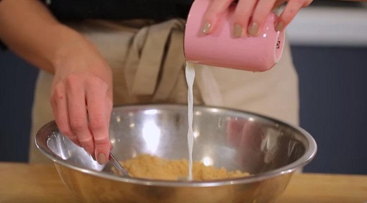 Fügen Sie Milch zu den Krümeln der Plätzchen hinzu und kneten Sie diese Masse.