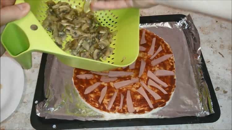 Um Pizza mit Wurst und Käse zuzubereiten, geben Sie die Füllung auf den Teig