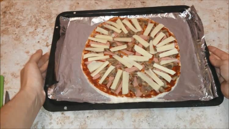 Um Pizza mit Wurst und Käse zuzubereiten, heizen Sie den Ofen vor