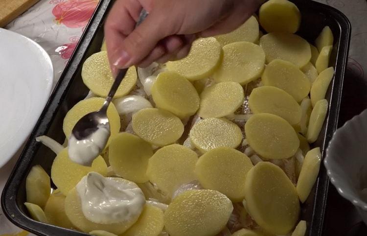 Per cuocere il merluzzo con le patate al forno, ungere le patate con panna acida