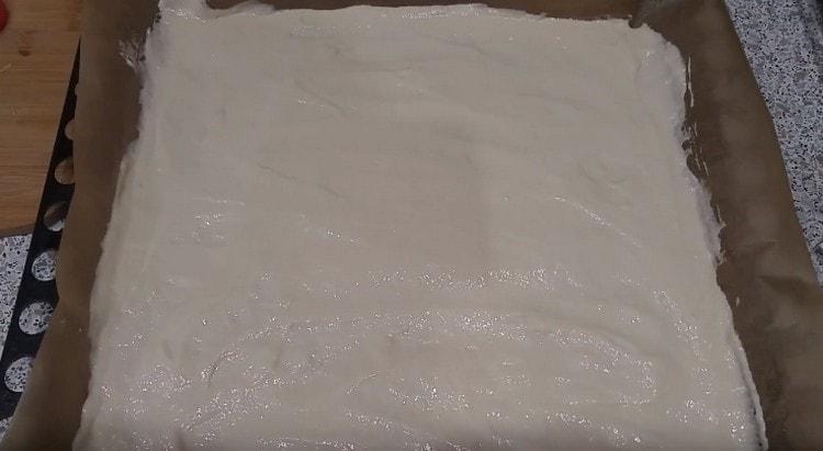 Тестото за пица, приготвено на кефир, се разпределя равномерно върху лист за печене, покрит с пергамент.