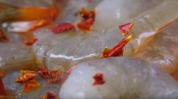 Krevečių svogūną paskleiskite česnaku, suberkite čili pipirus.