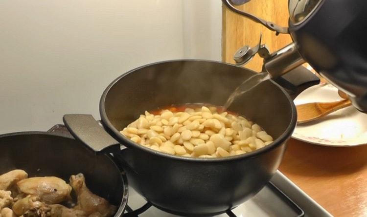 Прехвърляме сварения боб в доматен сос, добавяме вода.
