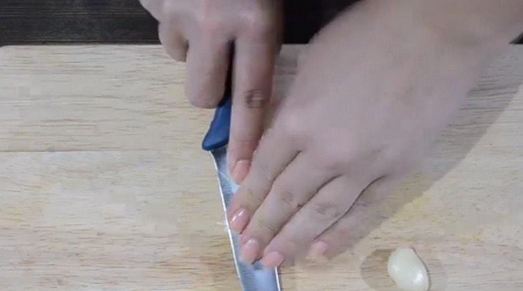 Den Knoblauch mit der flachen Seite des Messers zerdrücken.
