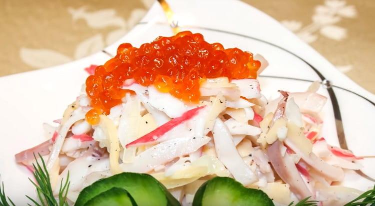 Kapag naglilingkod, ang salad na may mga calamari at crab sticks ay pinalamutian ng mga pulang caviar.