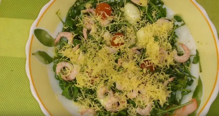 Fertiger Salat mit Rucola, Garnelen und Kirschtomaten mit geriebenem Käse bestreuen.
