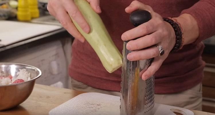 Reiben Sie die Zucchini auf einer Reibe und geben Sie sie in die Zwiebel.