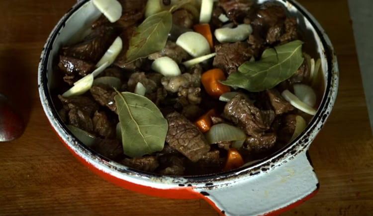 Přidejte smažené maso do zeleniny, přidejte česnek, bobkový list, koření.