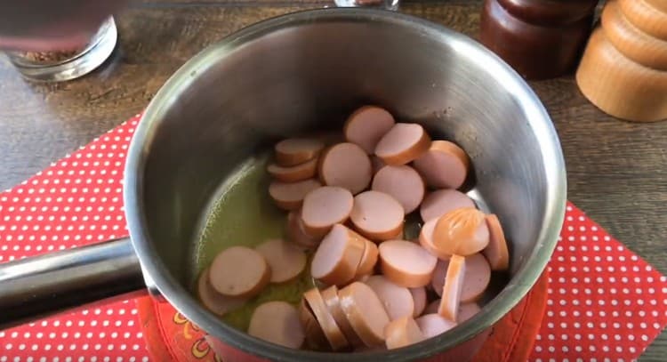 Нарежете колбасите на кръгчета и разстелете в тенджера.