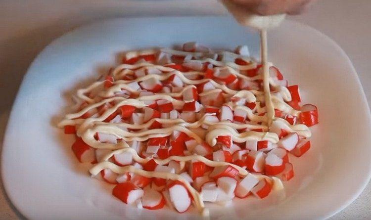 Ant plokštelės sudėkite krabų lazdelių sluoksnį, sutepkite majonezu.
