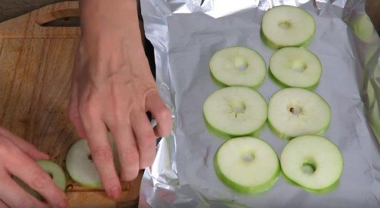 Schneiden Sie die Äpfel in dünne Kreise und verteilen Sie sie auf einem mit Folie bedeckten Backblech.