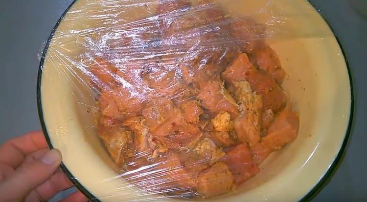 Eine Schüssel Fleisch mit Frischhaltefolie festziehen und marinieren lassen.