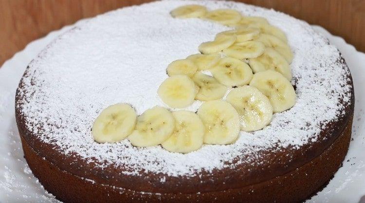Cospargere la torta di banane finita con zucchero a velo e decorare con fette di banana.