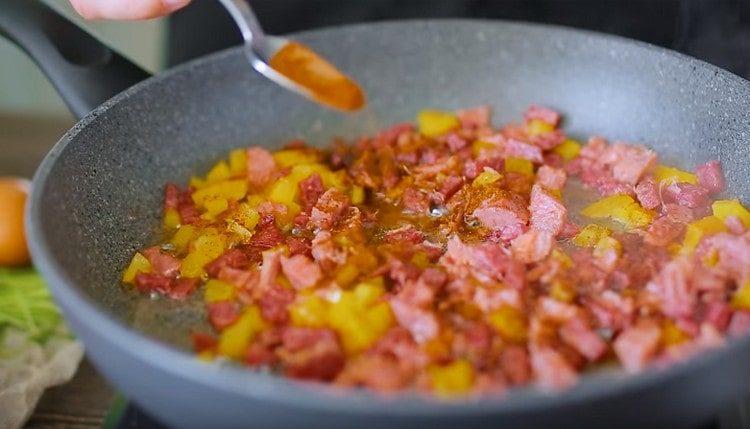 Λουκάνικο τηγανίζουμε με ζαμπόν, προσθέτουμε το ψιλοκομμένο πιπέρι και την πάπρικα.