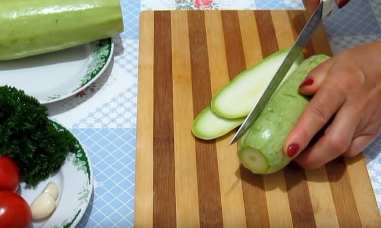 Die Zucchini in dünne Scheiben schneiden.