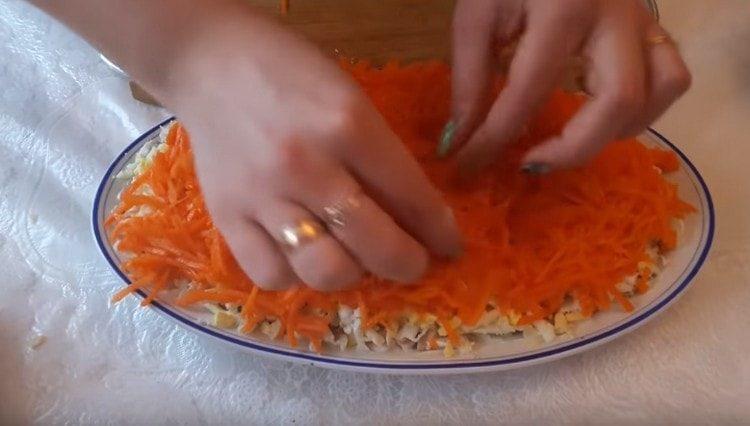 Smulkiai supjaustykite korėjiečių morkas ir iš jos suformuokite kitą salotų sluoksnį.